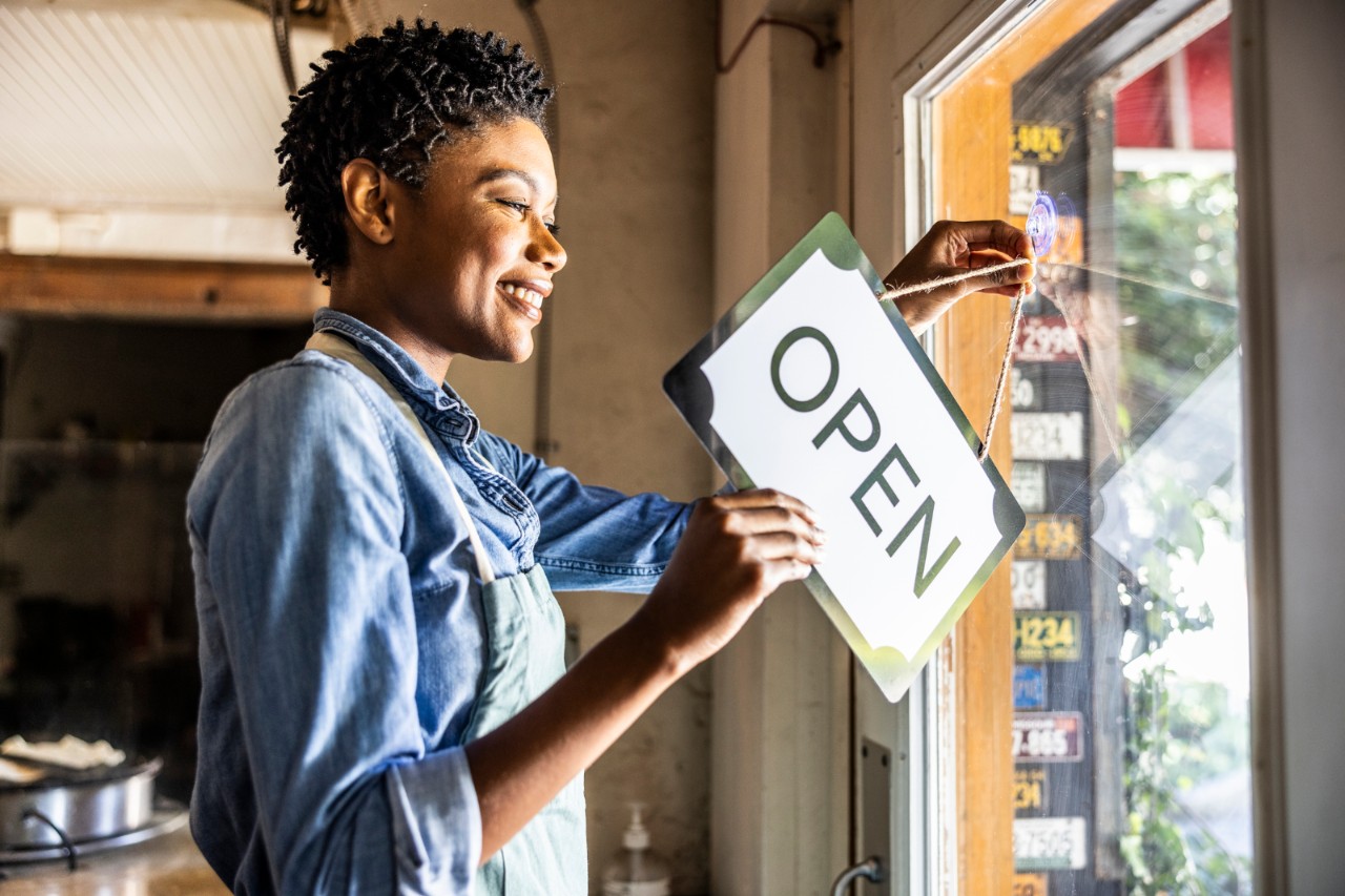 Female small business owner placing open sign in business window