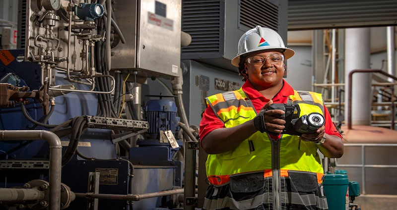 Erica conducts an inspection using a FLIR Thermal Imaging camera in an industrial setting, surrounded by machinery and equipment.