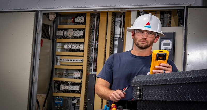 Jared uses a digital multimeter tester to inspect an electrical panel at Plant McIntosh, ensuring turbine system performance.